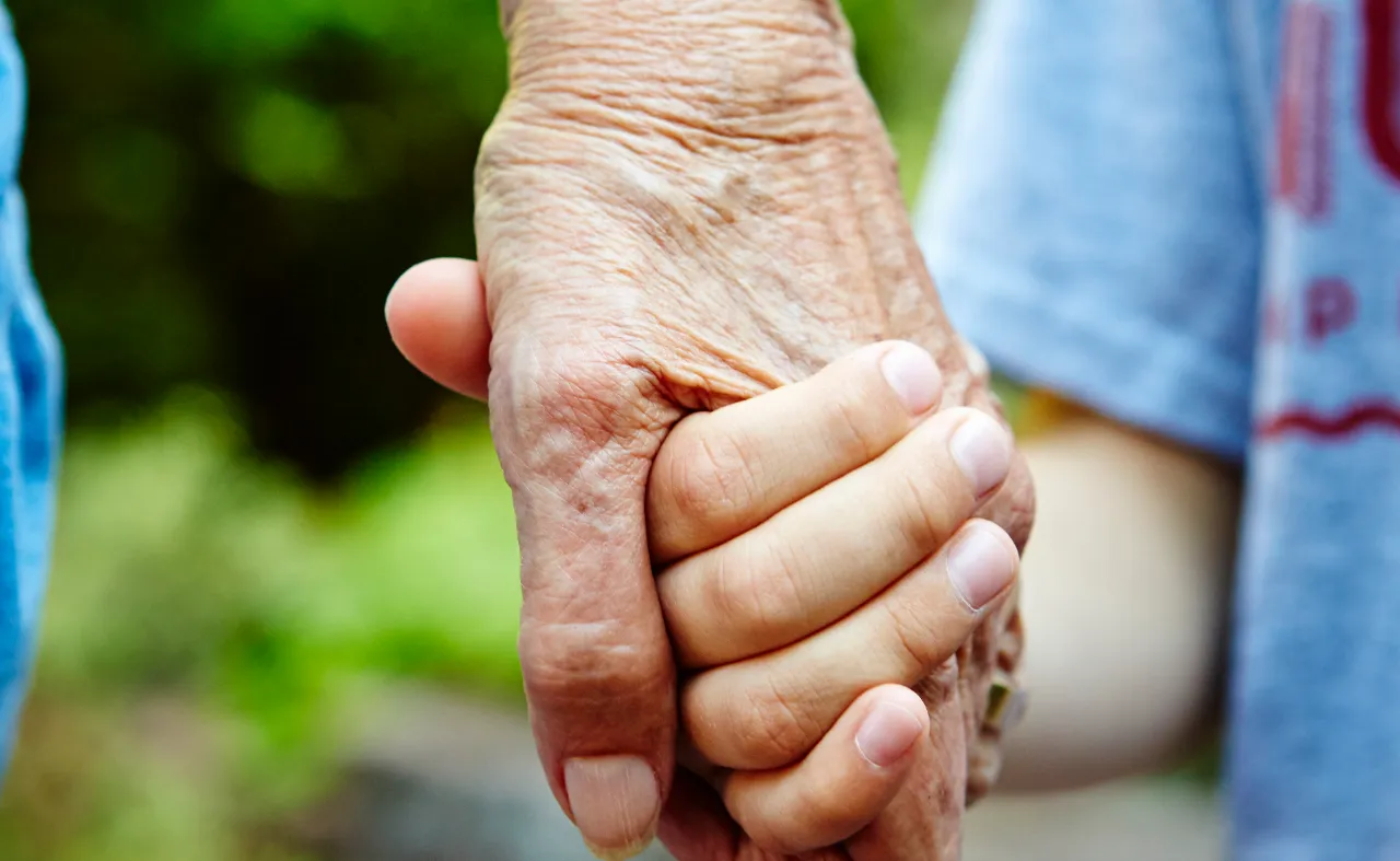 Young child holding elderly person's wrinkled hand outdoors
